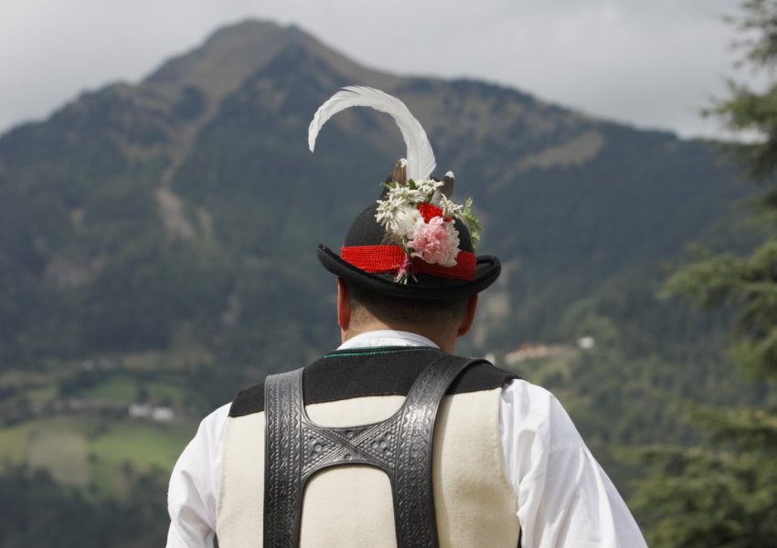 Dorf Tirol, Mann in Tracht vor Bergpanorama
